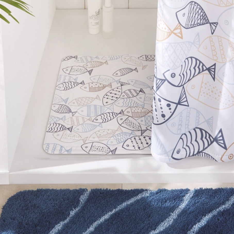 Badezimmer mit Duschvorleger und Duschvorhang im maritimen Fischdesign neben blauem Badteppich.