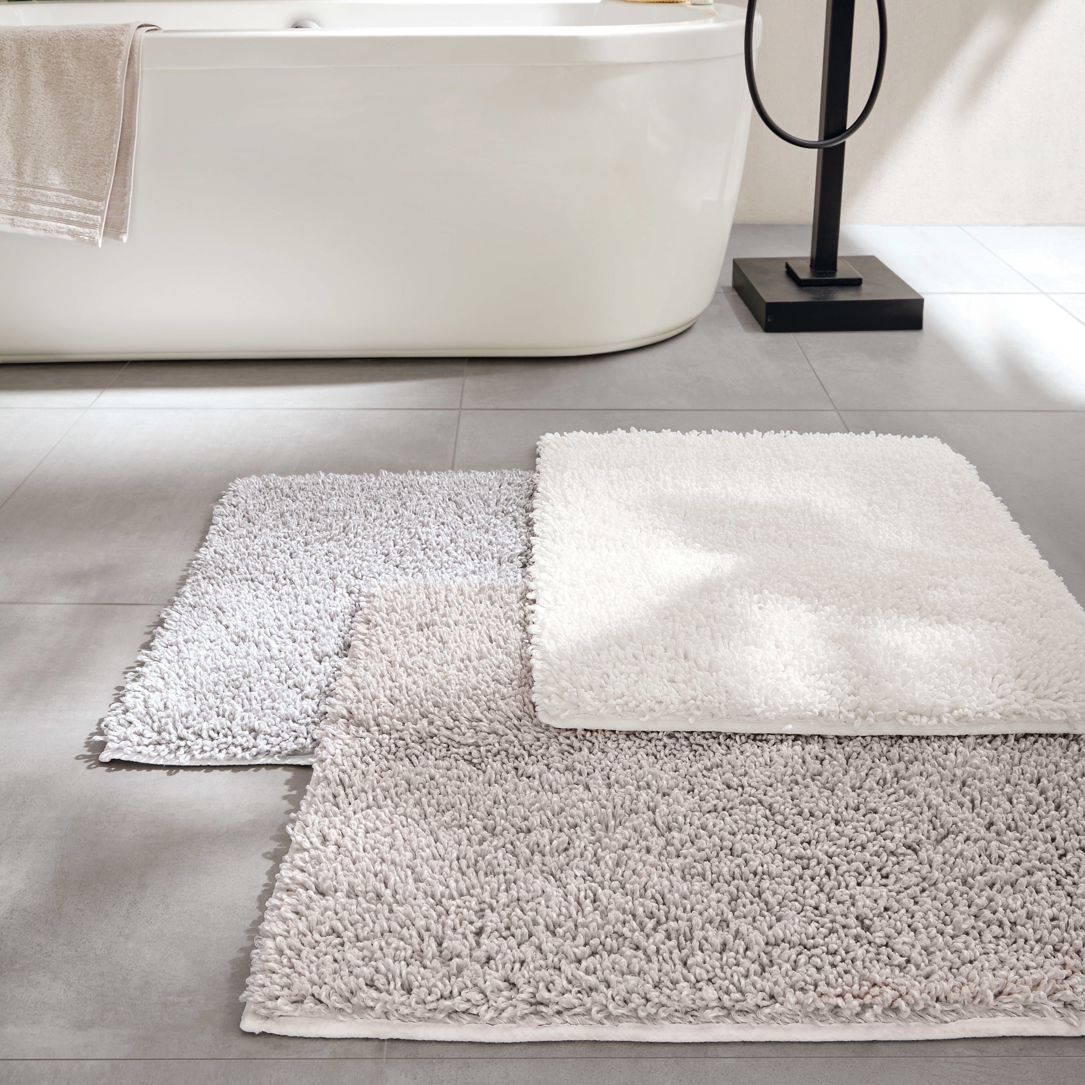 Drei Kleine Wolke Badteppiche in hellen Farben liegen nebeneinander im modernen Bad.