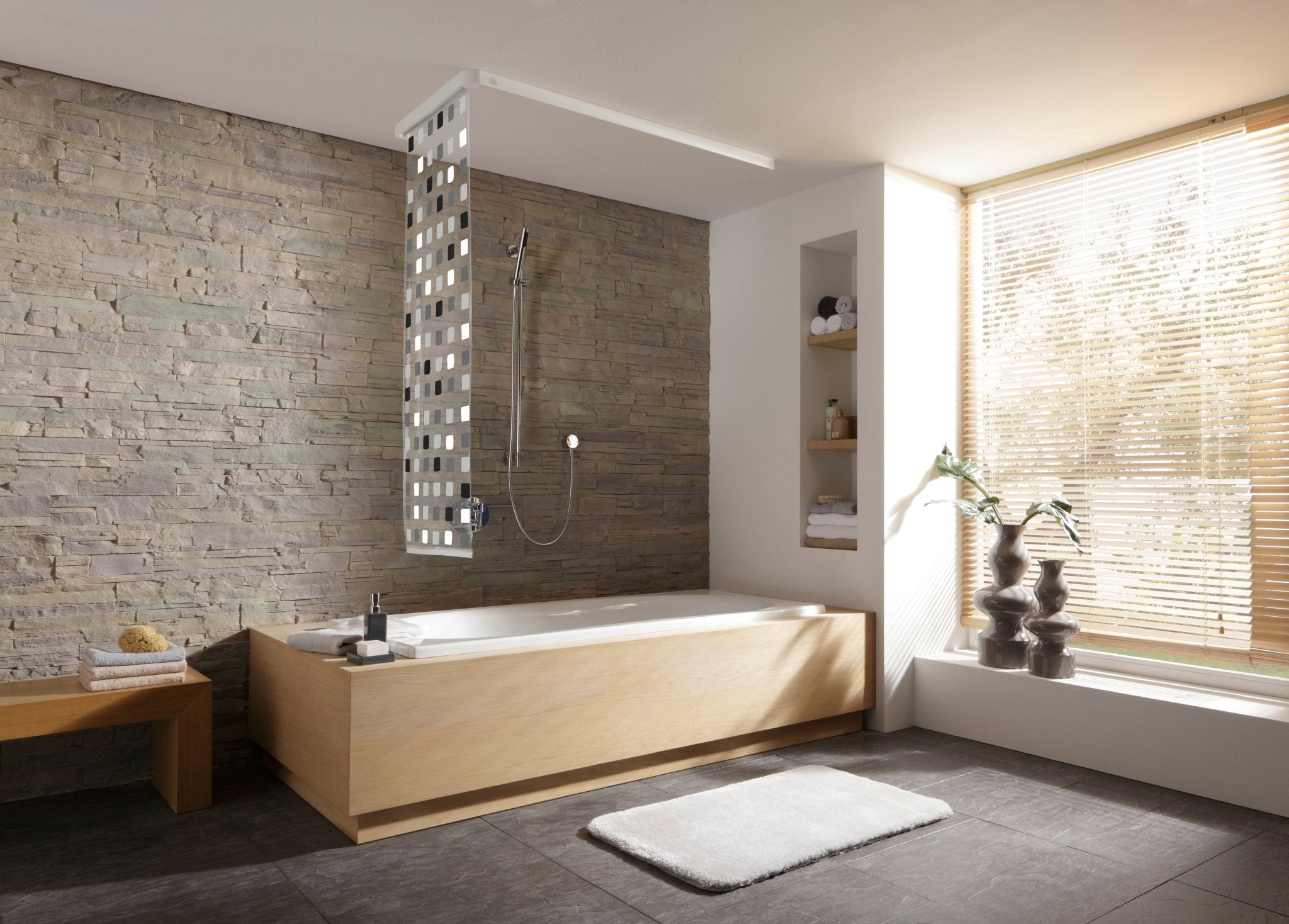 Schmaler grauer Duschrollo an Badewanne in modernem Bad mit Steinwand und Fenster mit Jalousie.