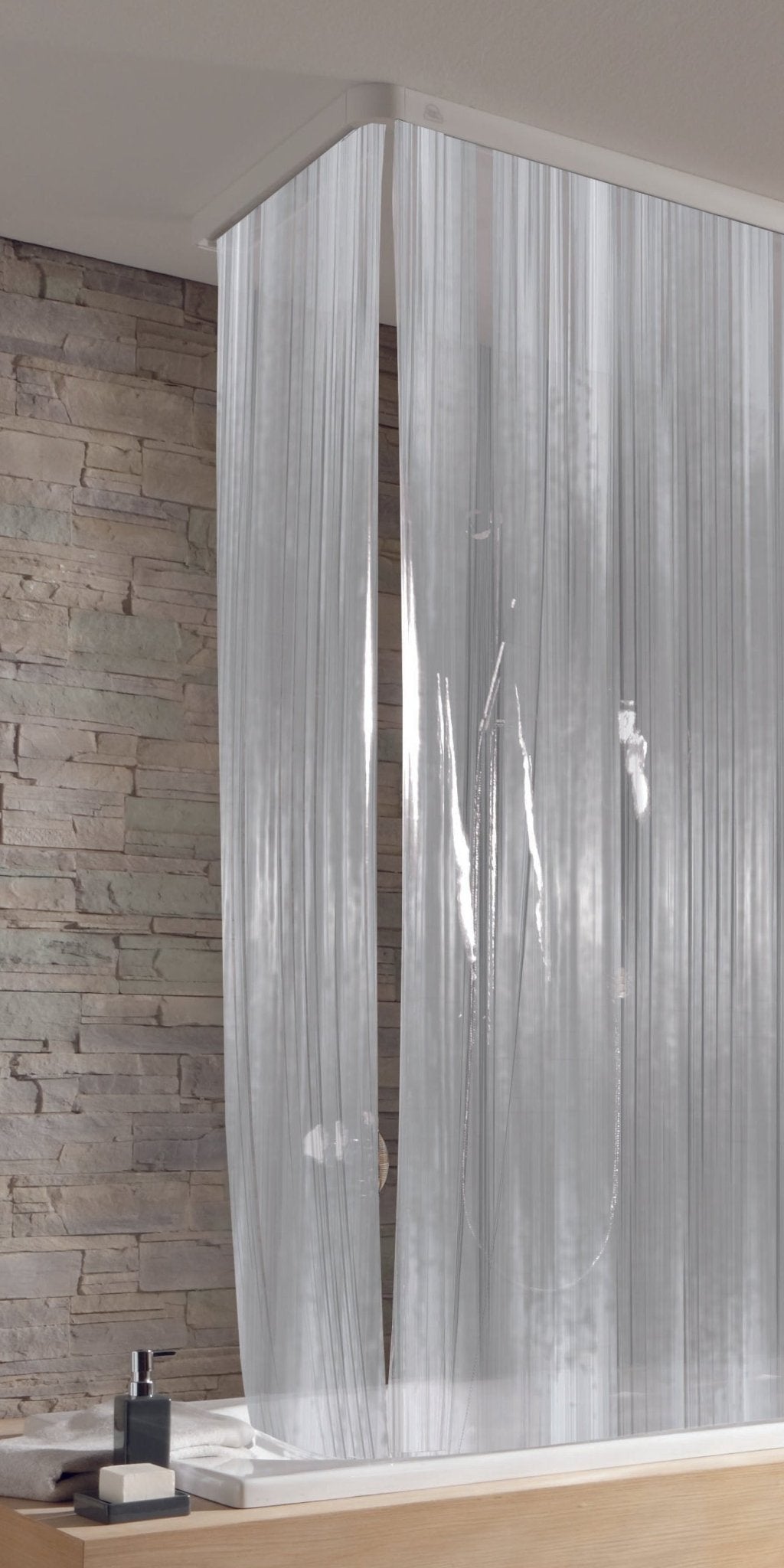 Schmaler Duschrollo Milky in transparenter Ausführung hängt vor einer Steinwand in der Dusche.