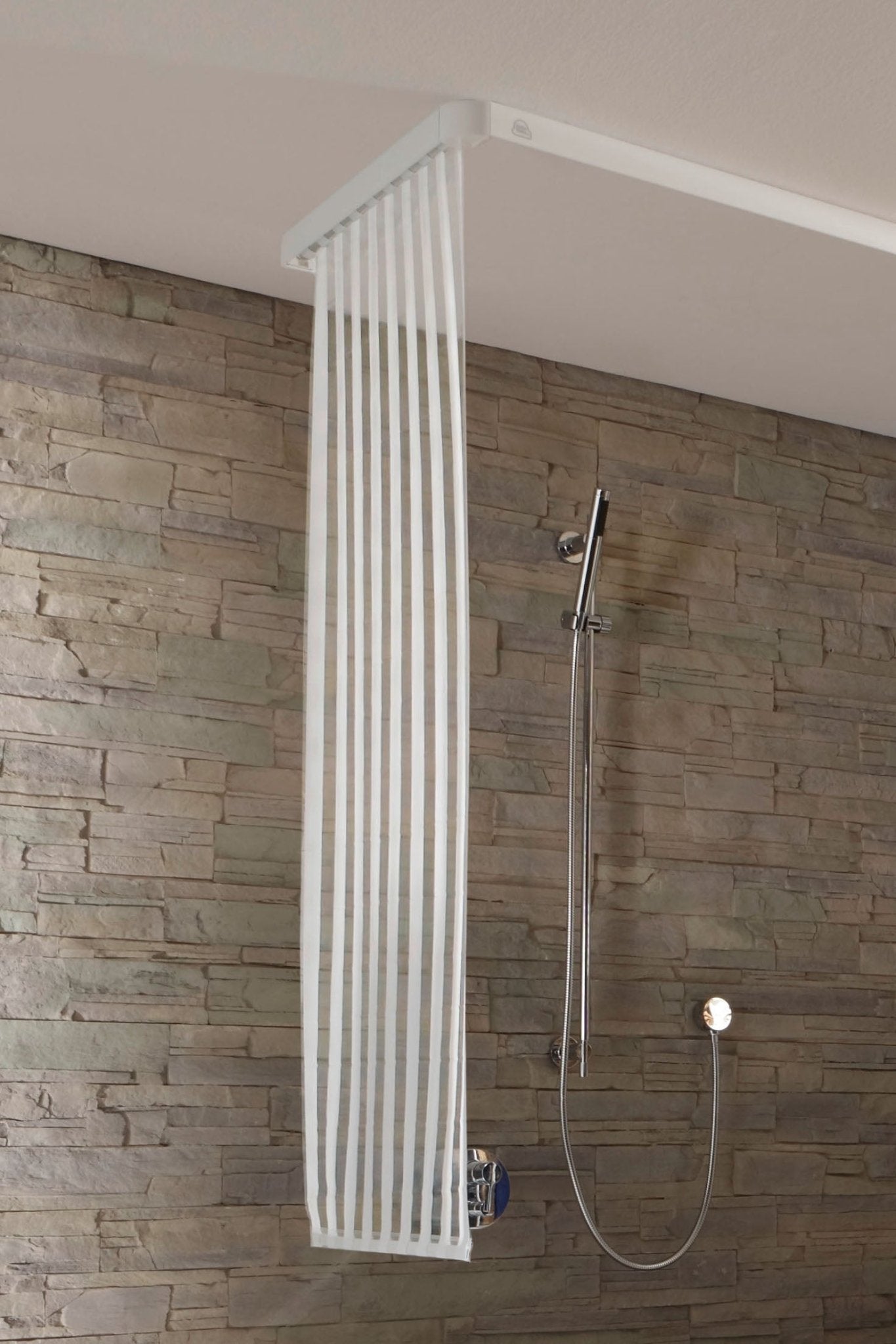 Schmaler weißer Duschrollo für kleine Leerkassette in moderner Dusche vor Steinwand montiert.
