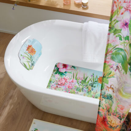 Freistehende Badewanne mit floralem Badteppich, Kissen und Duschvorhang.