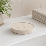 Beige Seifenschale steht auf dem Waschbecken neben Pflanze und Handtüchern.