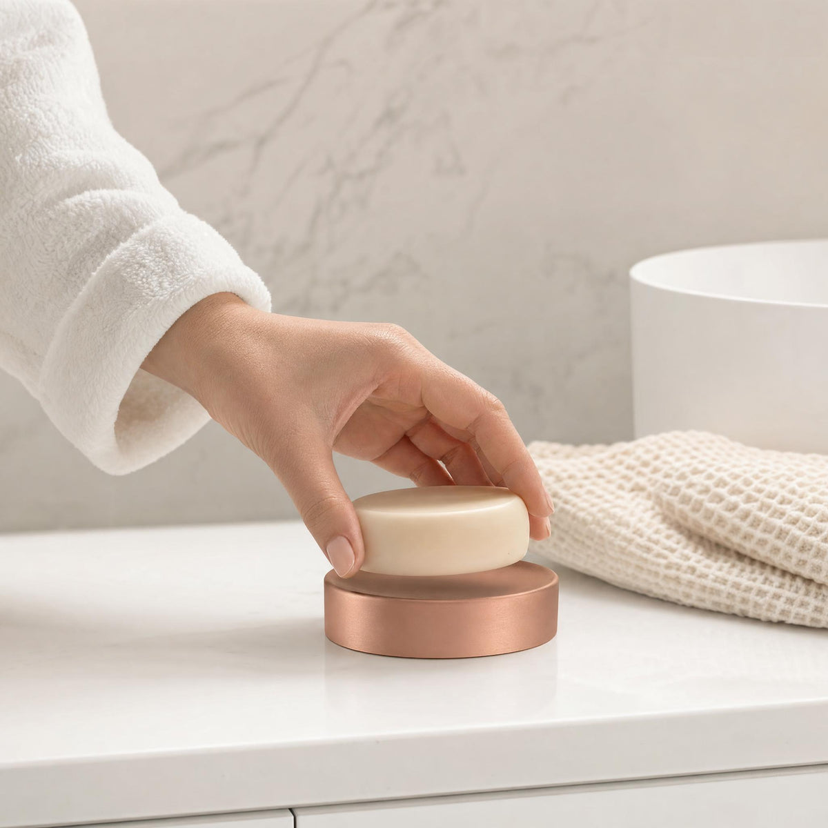 Hand legt Seife auf roségoldfarbene Seifenschale im hellen Badezimmer.