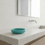 Türkise Seifenschale auf hellem Waschtisch vor Wandarmatur und Spiegel