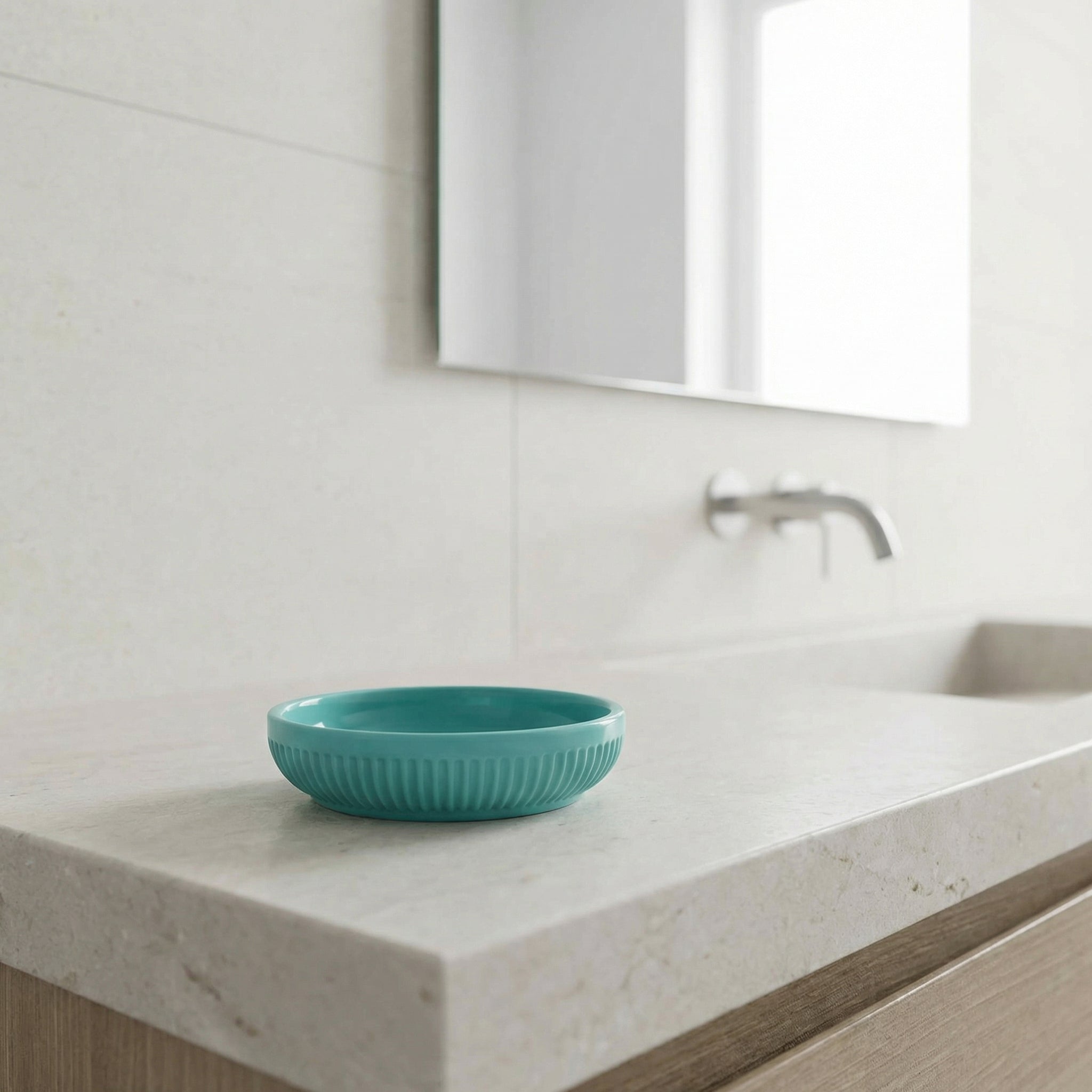 Türkise Seifenschale auf hellem Waschtisch vor Wandarmatur und Spiegel