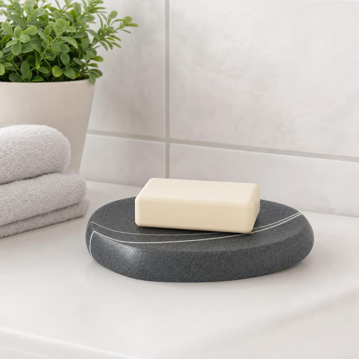 Eine dunkle Seifenschale mit heller Seife steht im Bad neben Handtüchern.