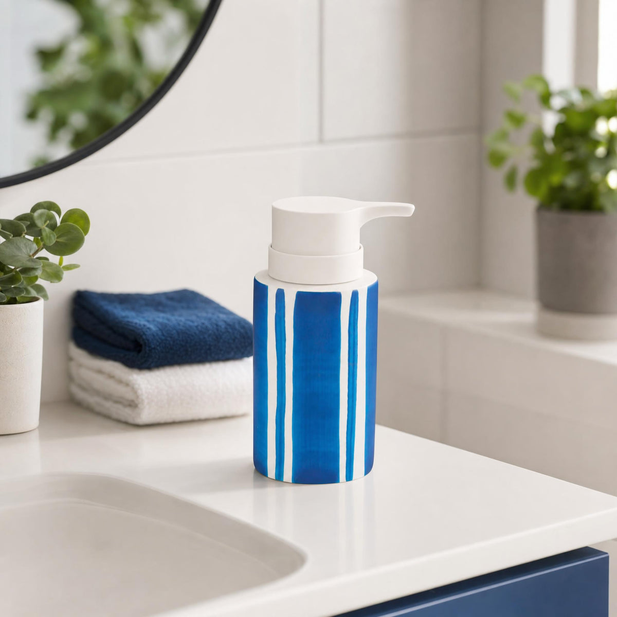 Blau-weißer Seifenspender auf Waschbecken mit Handtüchern und Pflanzen.