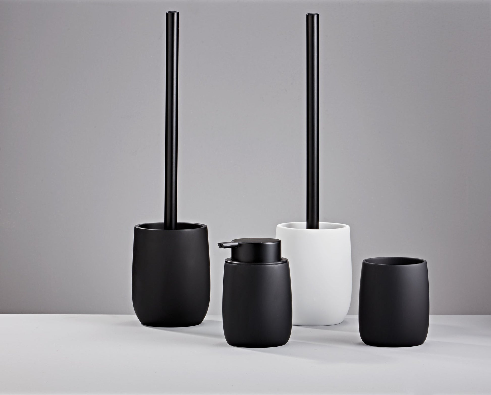 Seifenspender BONNY Schwarz steht mit passenden Badaccessoires vor grauem Hintergrund.