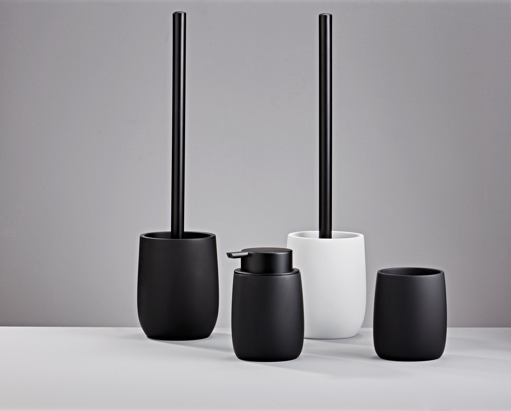 Seifenspender BONNY Schwarz steht mit passenden Badaccessoires vor grauem Hintergrund.
