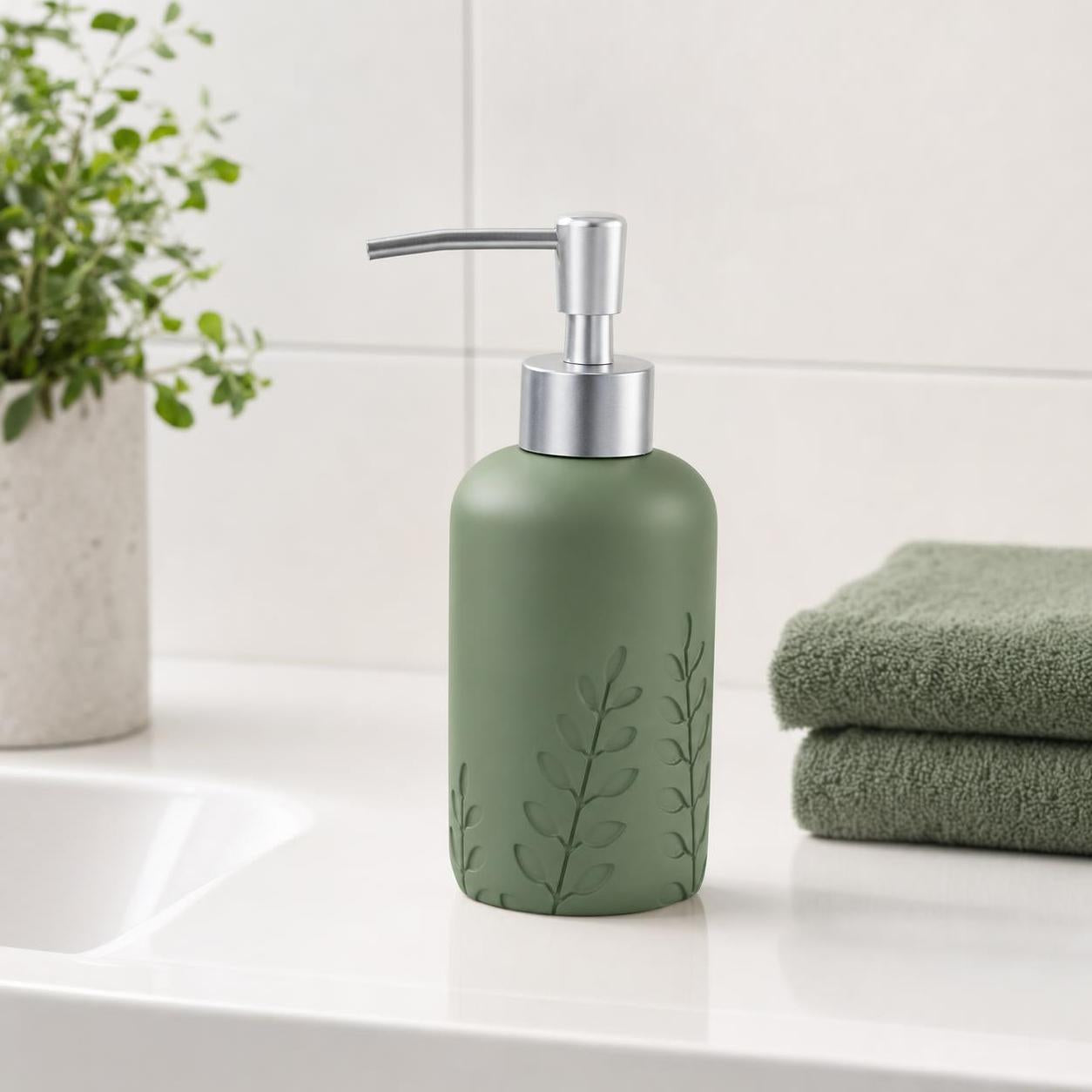 Grüner Seifenspender mit Blattrelief steht neben Handtüchern am Waschbecken.