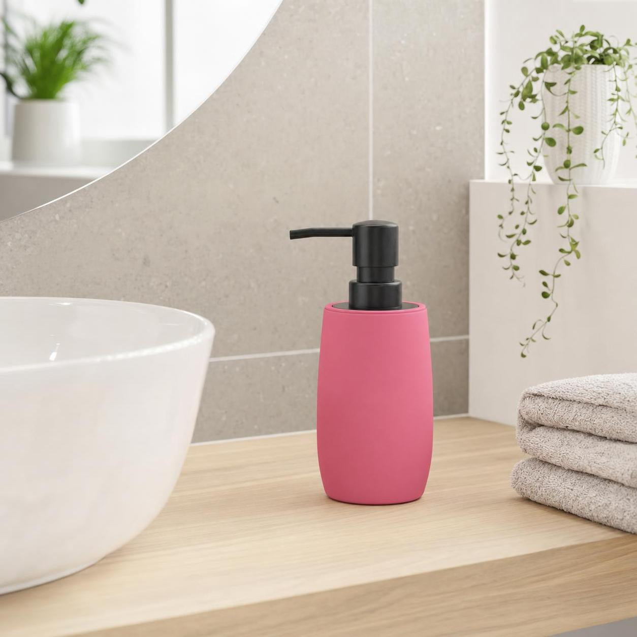 Ein pinker Seifenspender steht neben Waschbecken und Handtüchern im Bad.
