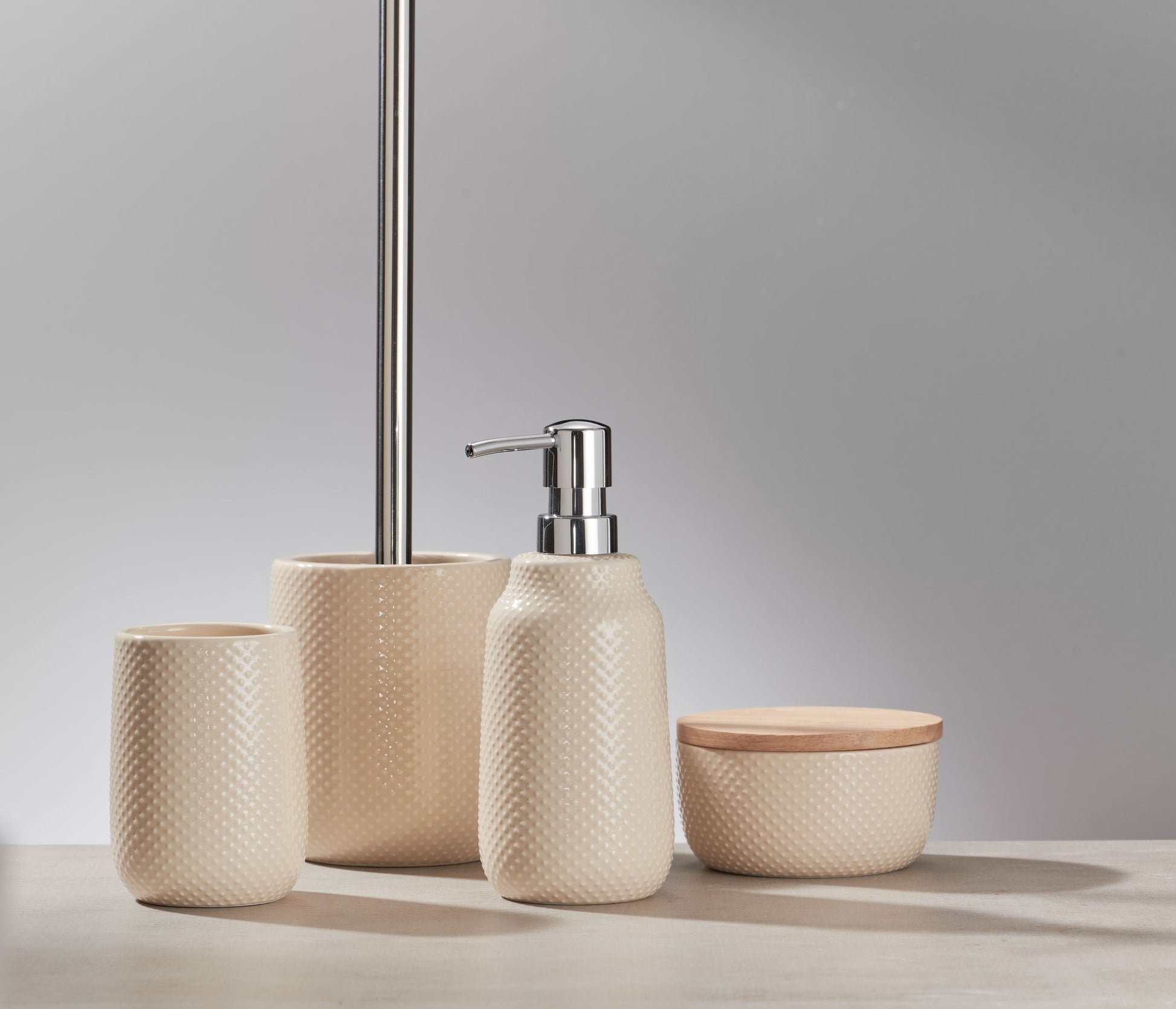 Beiges Badaccessoire-Set mit Spender, Bechern und Dose auf Holztisch