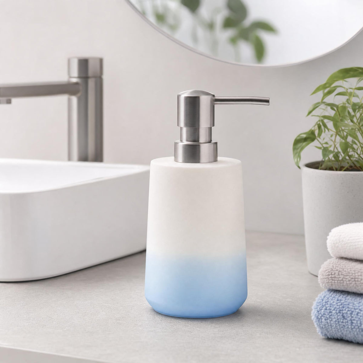 Seifenspender in Weiß-Blau auf Waschtisch neben Pflanze und Handtüchern.