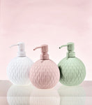 Drei runde Seifenspender in Weiß, Rosa und Grün vor rosa Hintergrund