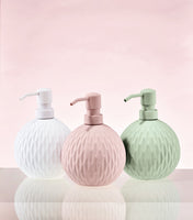 Drei runde Seifenspender in Weiß, Rosa und Grün vor rosa Hintergrund