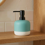 Türkiser Seifenspender mit schwarzem Pumpkopf auf Holzablage im Badregal