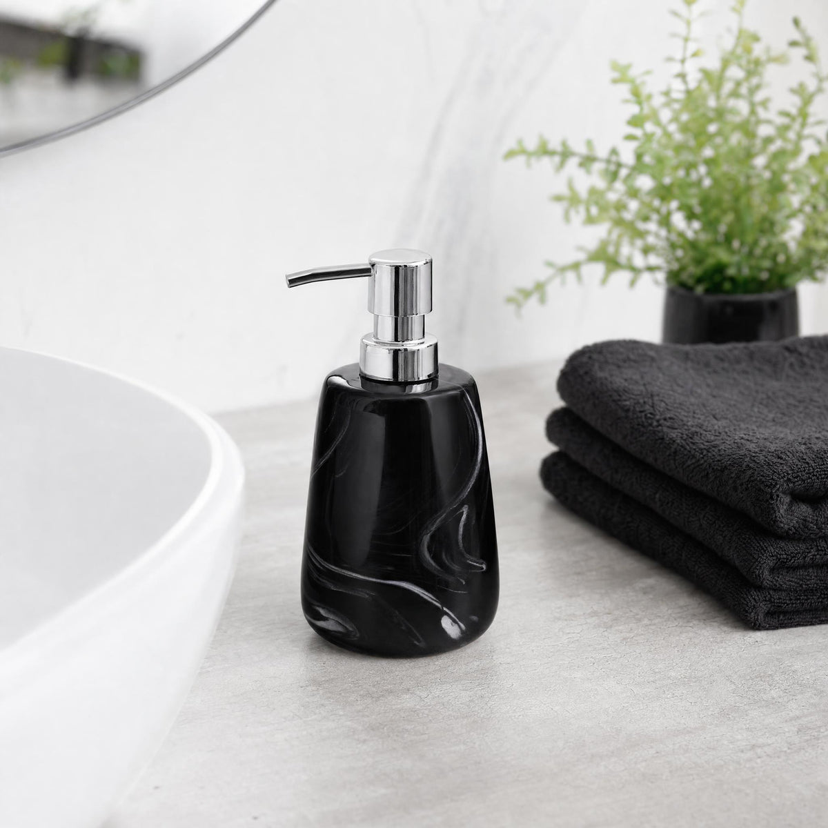Schwarzer Seifenspender neben Waschbecken, Handtüchern und Pflanze.