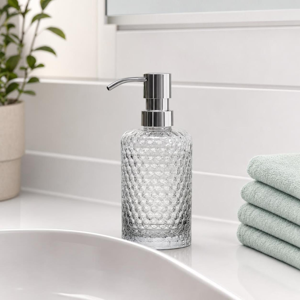 Ein transparenter Glas-Seifenspender mit Chrompumpe steht am Waschbecken.