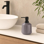Violettgrauer Seifenspender mit schwarzer Pumpe steht am Waschbecken.