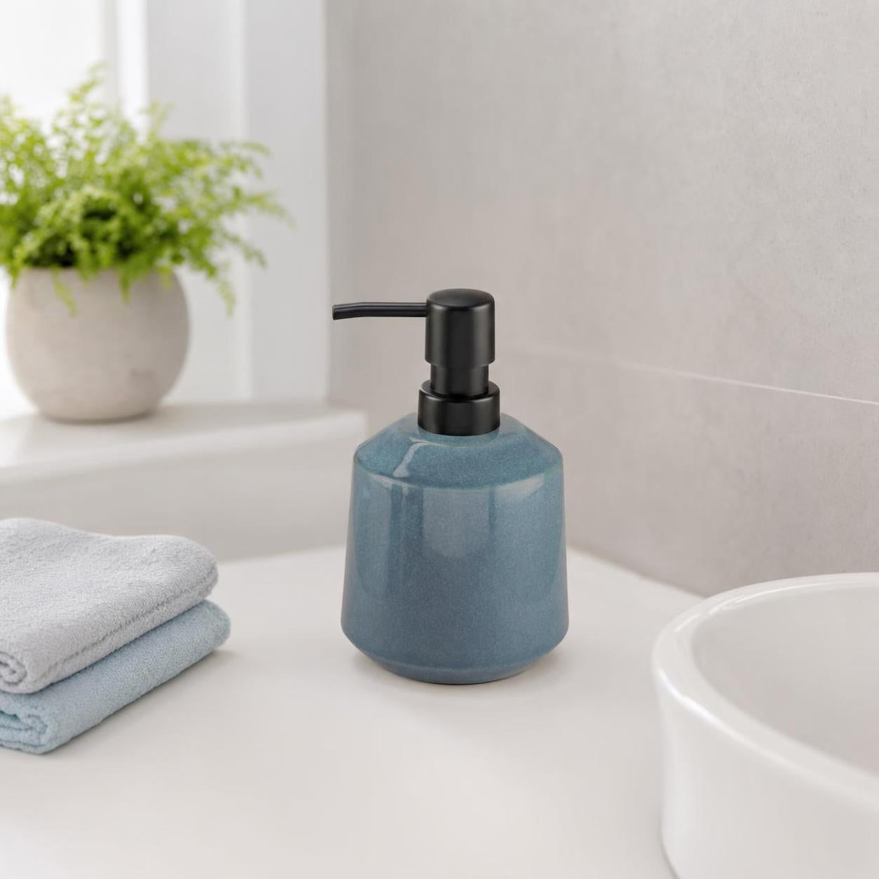 Ein blauer Seifenspender steht neben Handtüchern am Waschbecken.