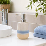 Beige-blauer Keramik-Seifenspender mit Chrompumpe steht am Waschbecken.
