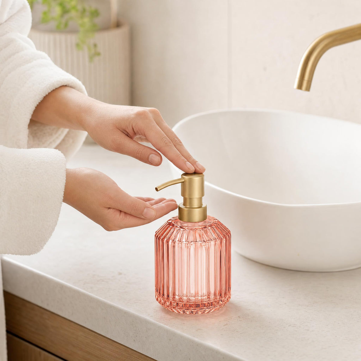 Hand betätigt rosa Seifenspender aus Glas am Waschbecken im Bad.