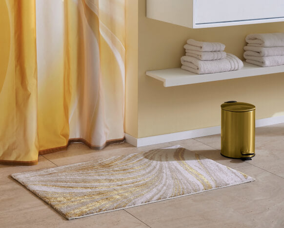 Badezimmer mit Badematte, Vorhang und Eimer in goldfarbenen Tönen.