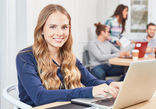 Junge Frau arbeitet lächelnd mit Laptop in modernem Ausbildungsbüro.