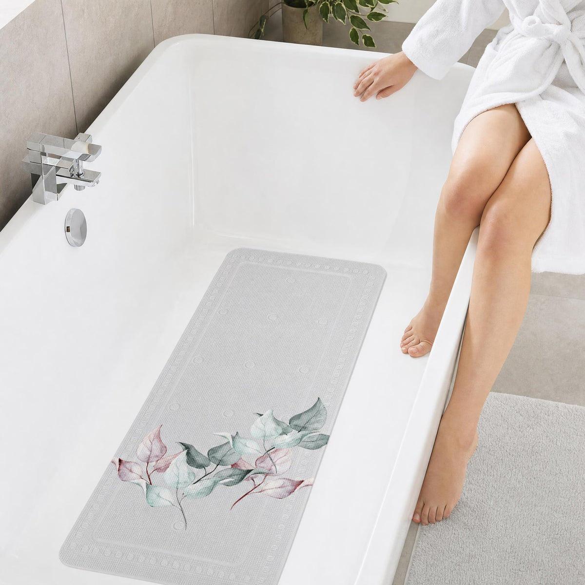 Antirutschmatte mit Blättermuster in weißer Wanne neben Person im Bademantel.