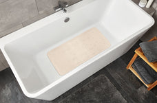 Weiße Badewanne mit beiger Antirutschmatte und grauer Badematte daneben