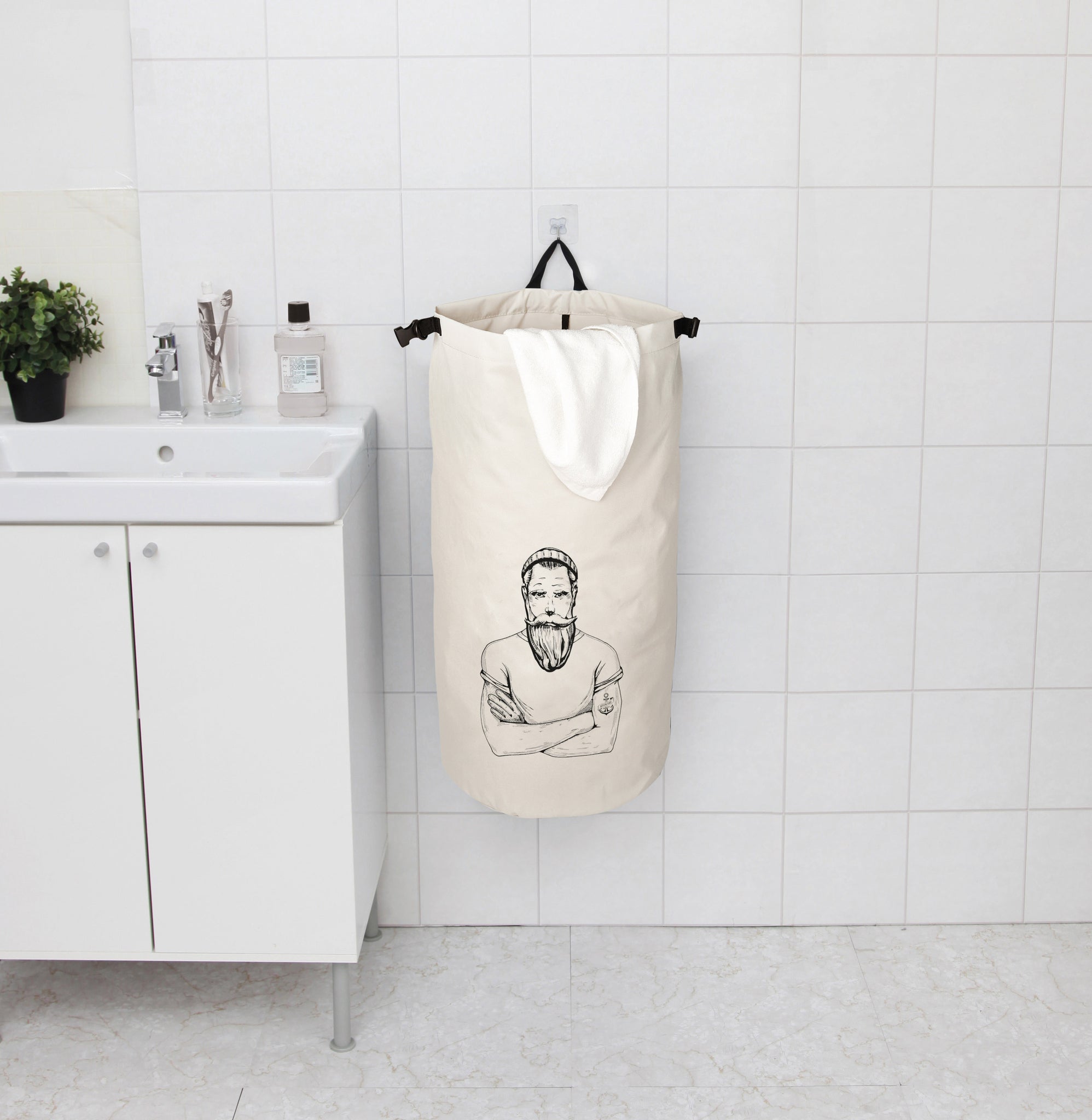 Beiger Wäschesack mit Druck, Handtuch und Waschbecken im Bad an Wand