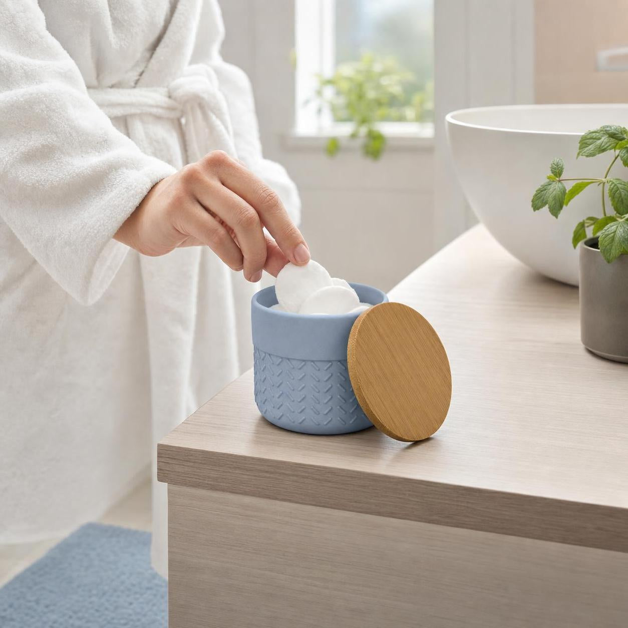 Eine Hand greift Wattepads aus einer blauen Dose mit Bambusdeckel.