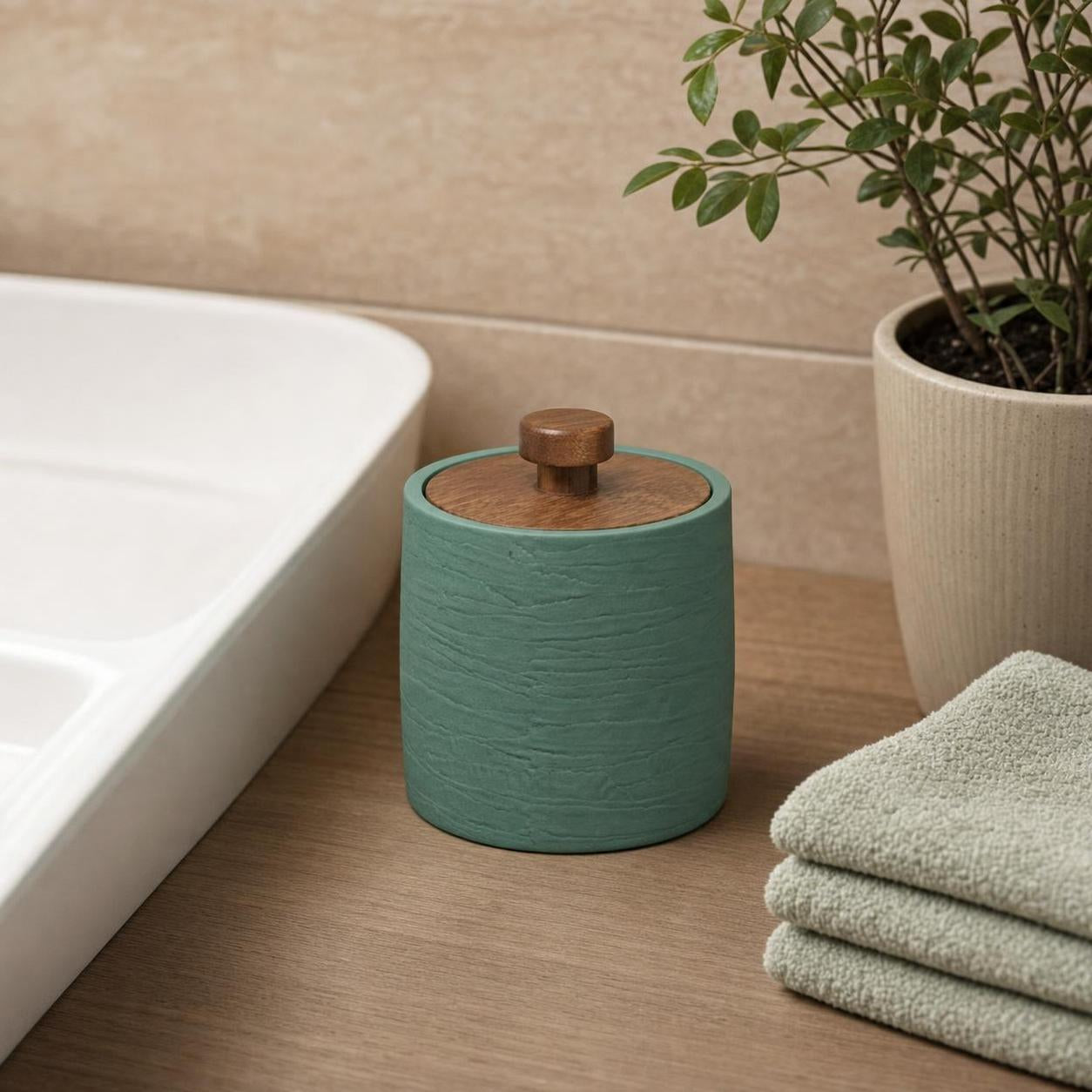 Grüne Aufbewahrungsdose mit Holzdeckel steht neben Handtüchern im Bad.