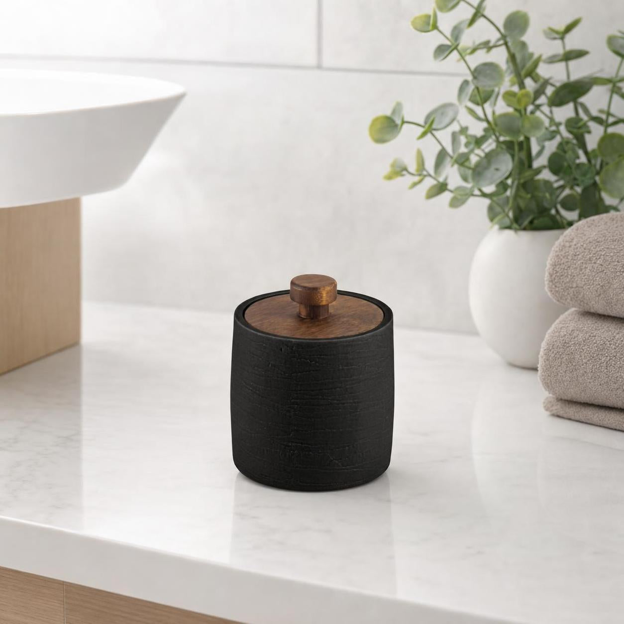 Schwarze Dose mit Holzdeckel steht auf einem Marmorwaschtisch.
