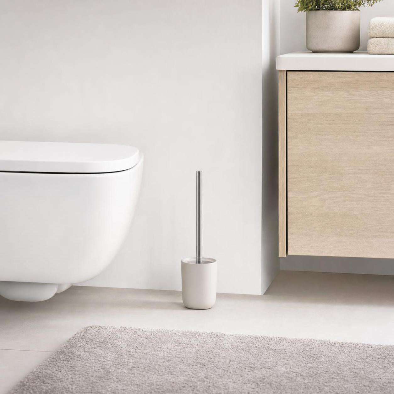Weiße WC-Bürste mit Chromgriff steht neben Toilette und Badschrank.