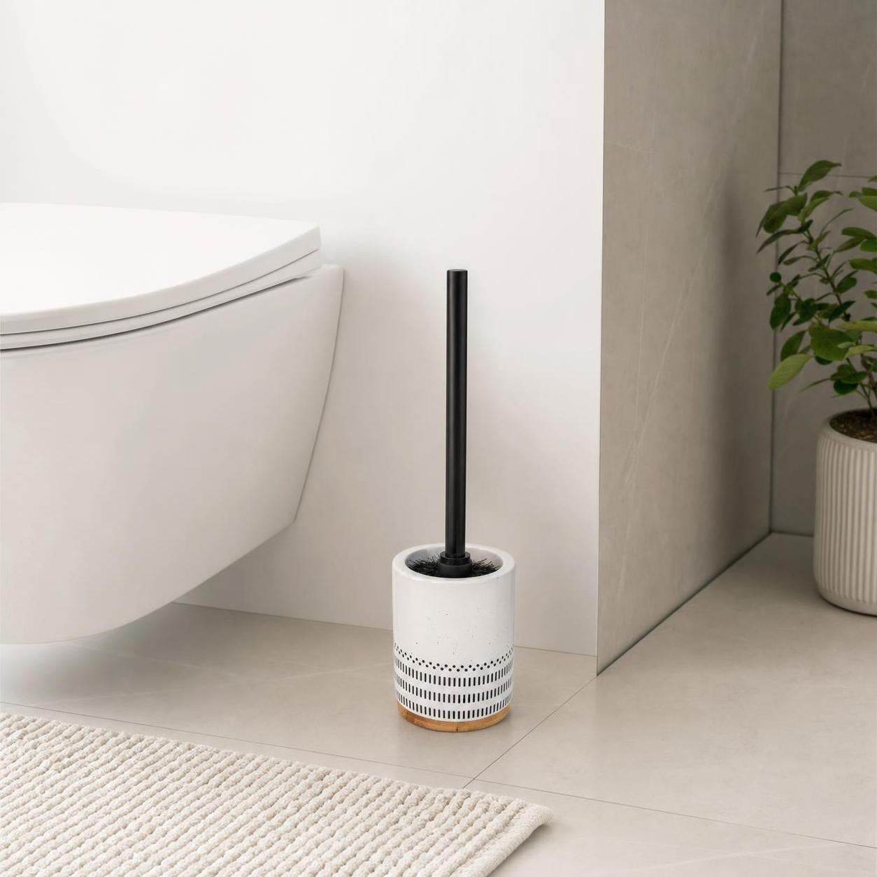 Eine WC-Bürste mit schwarzem Griff steht im weißen Halter neben der Toilette.