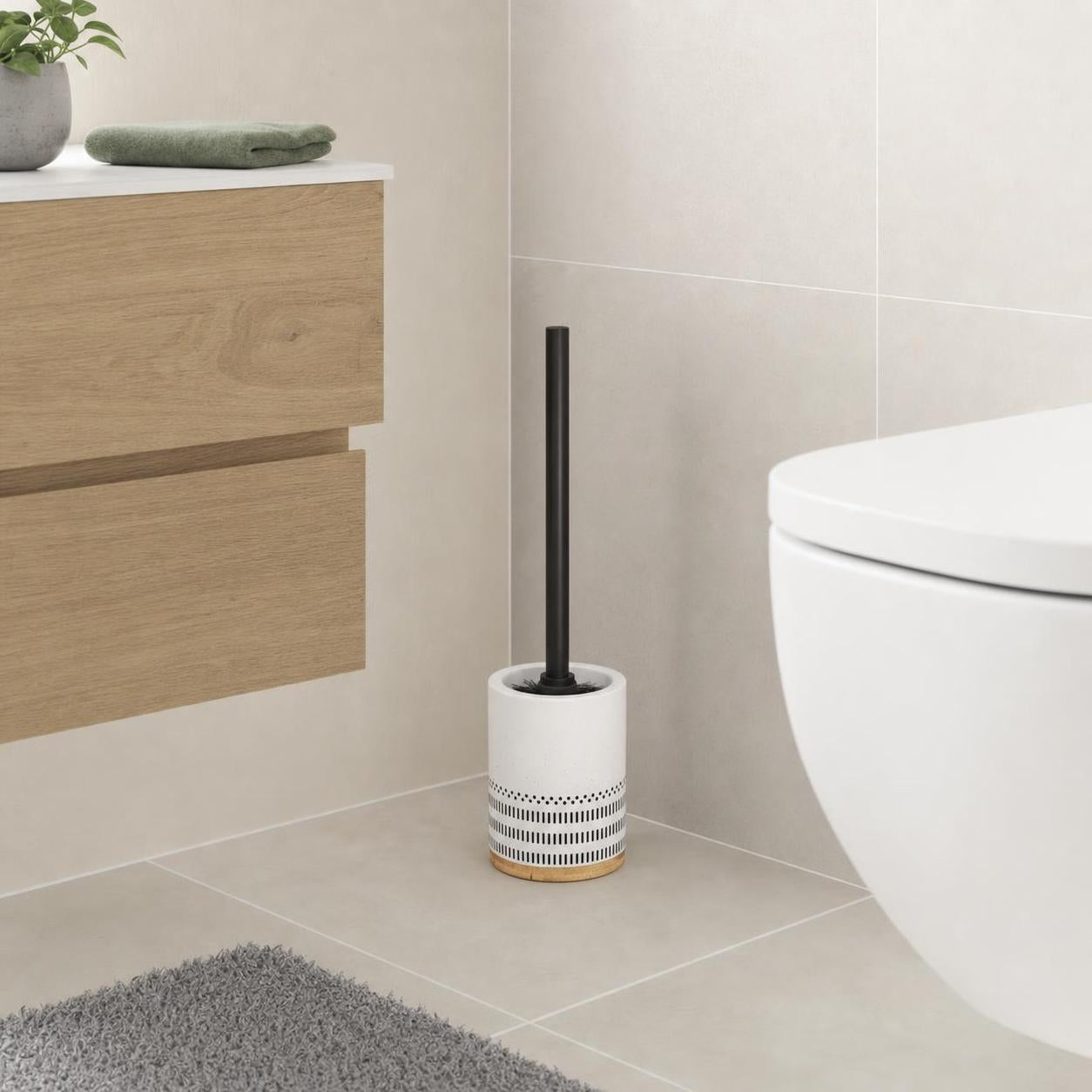 Eine schwarze Toilettenbürste steht im weißen Halter mit Holzfuß.