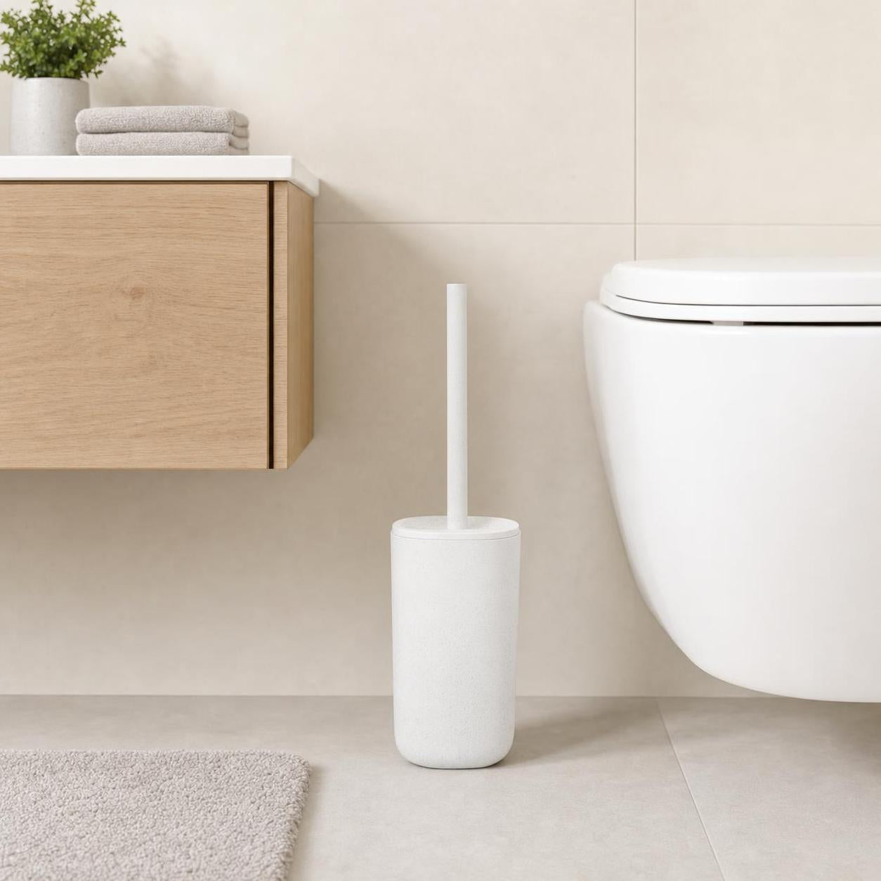 Weiße WC-Bürste mit Halter steht neben der Toilette im hellen Bad.