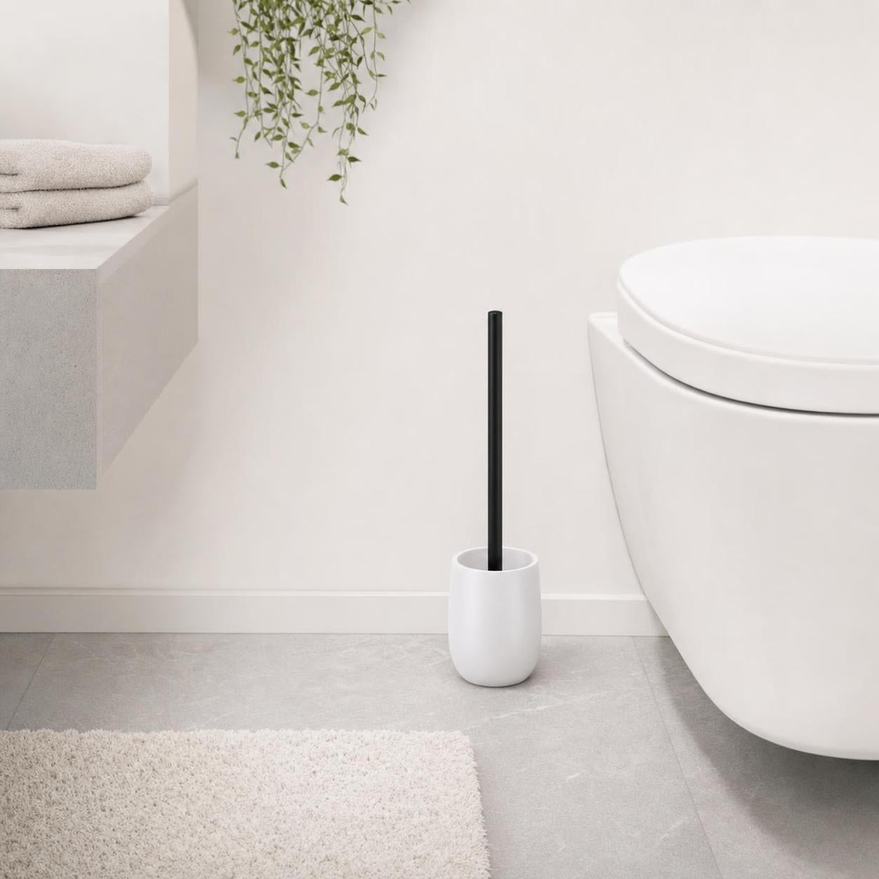 Weiße WC-Bürste mit schwarzem Griff steht neben der Toilette.
