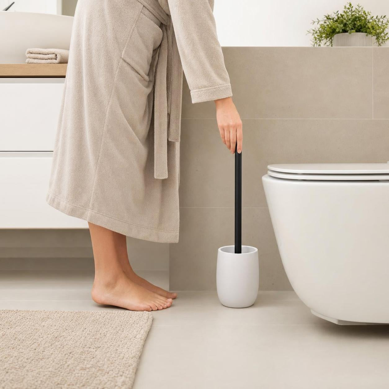 Eine WC-Bürste mit weißem Halter steht neben der Toilette im Bad.
