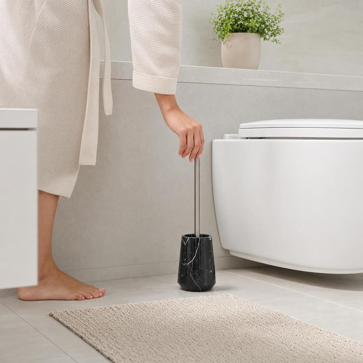 Eine schwarze WC-Bürste im Marmorhalter steht neben der Toilette.