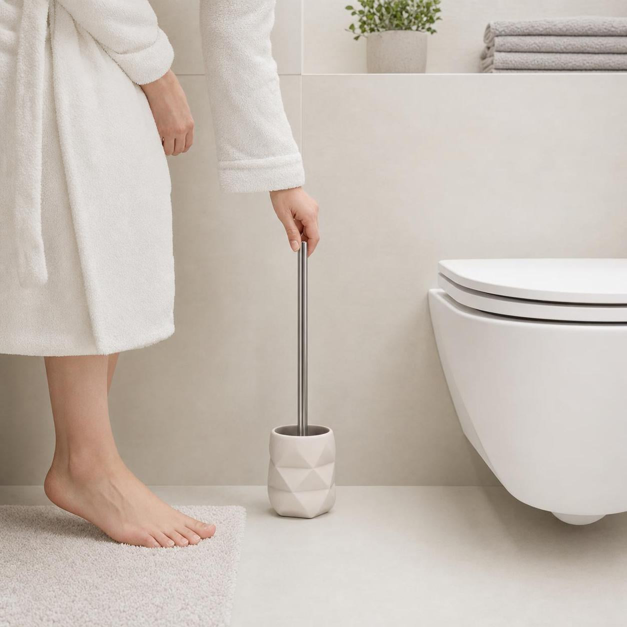 Eine Hand greift zur WC-Bürste im weißen Halter neben der Toilette.