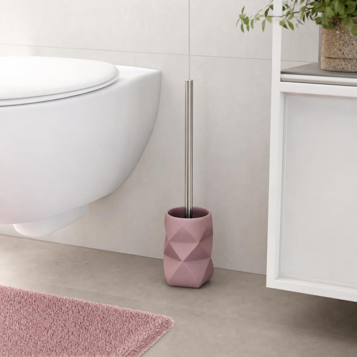 Rosa WC-Bürste mit facettiertem Halter steht neben der Toilette.