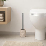 Beige WC-Bürste mit Chromgriff steht neben einer weißen Toilette.