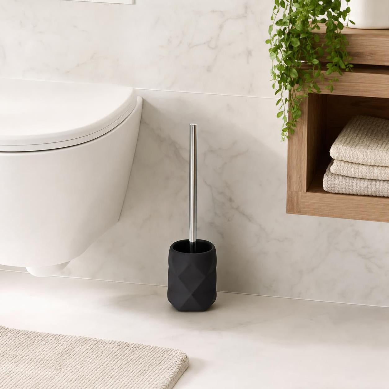 Schwarze WC-Bürste mit Chromgriff steht neben der Toilette im Bad.