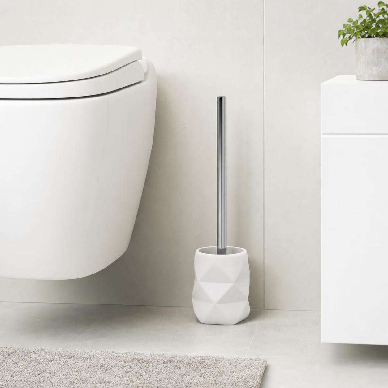 Weiße WC-Bürste im facettierten Halter steht neben der Toilette.