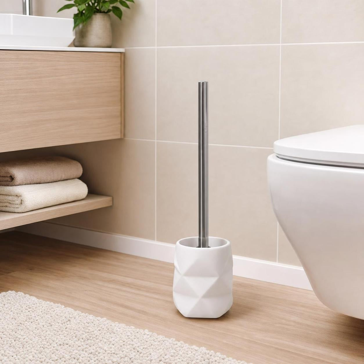 Weiße WC-Bürste mit Edelstahlgriff steht neben der Toilette im Bad.