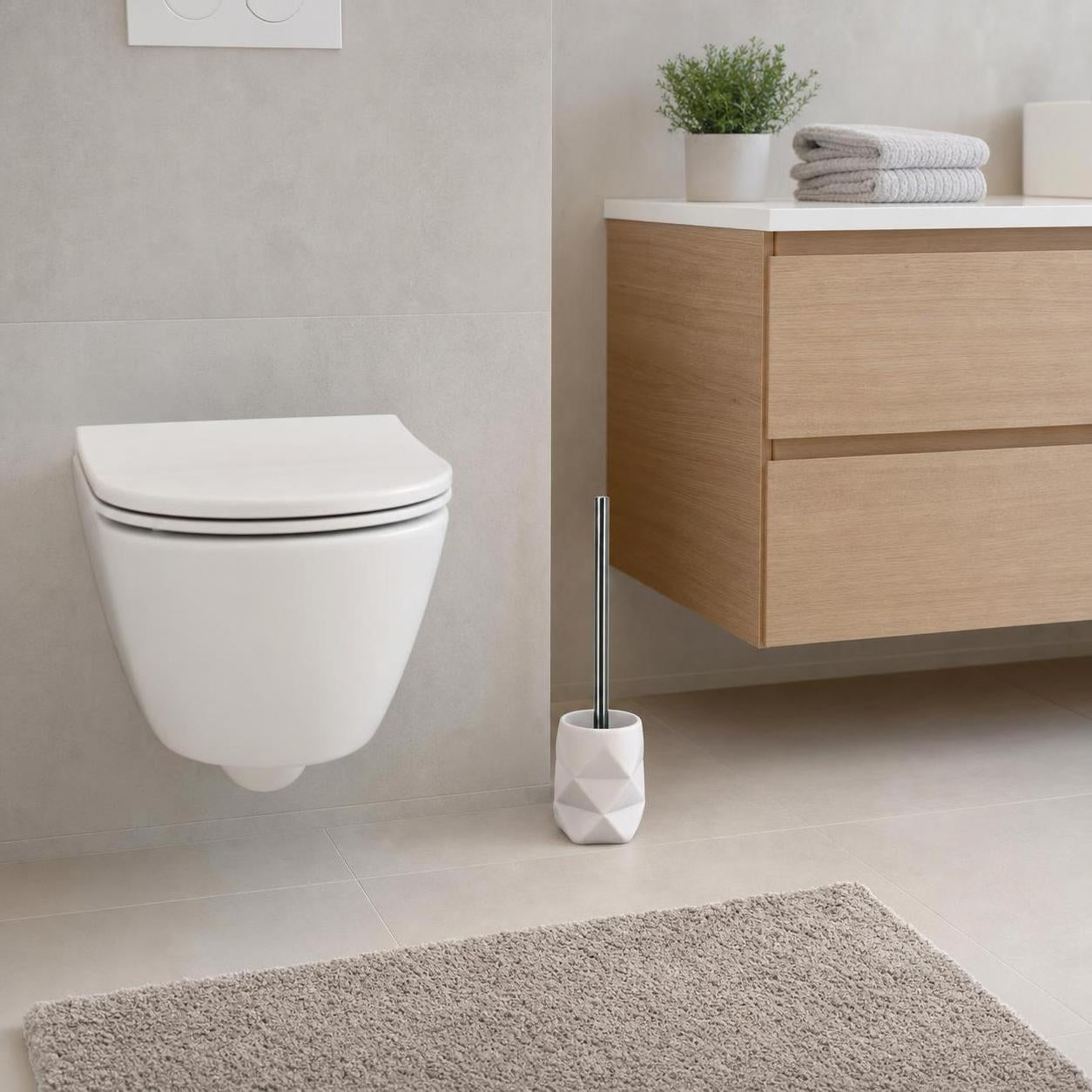 Weiße WC-Bürste im facettierten Halter steht neben Toilette und Waschtisch.