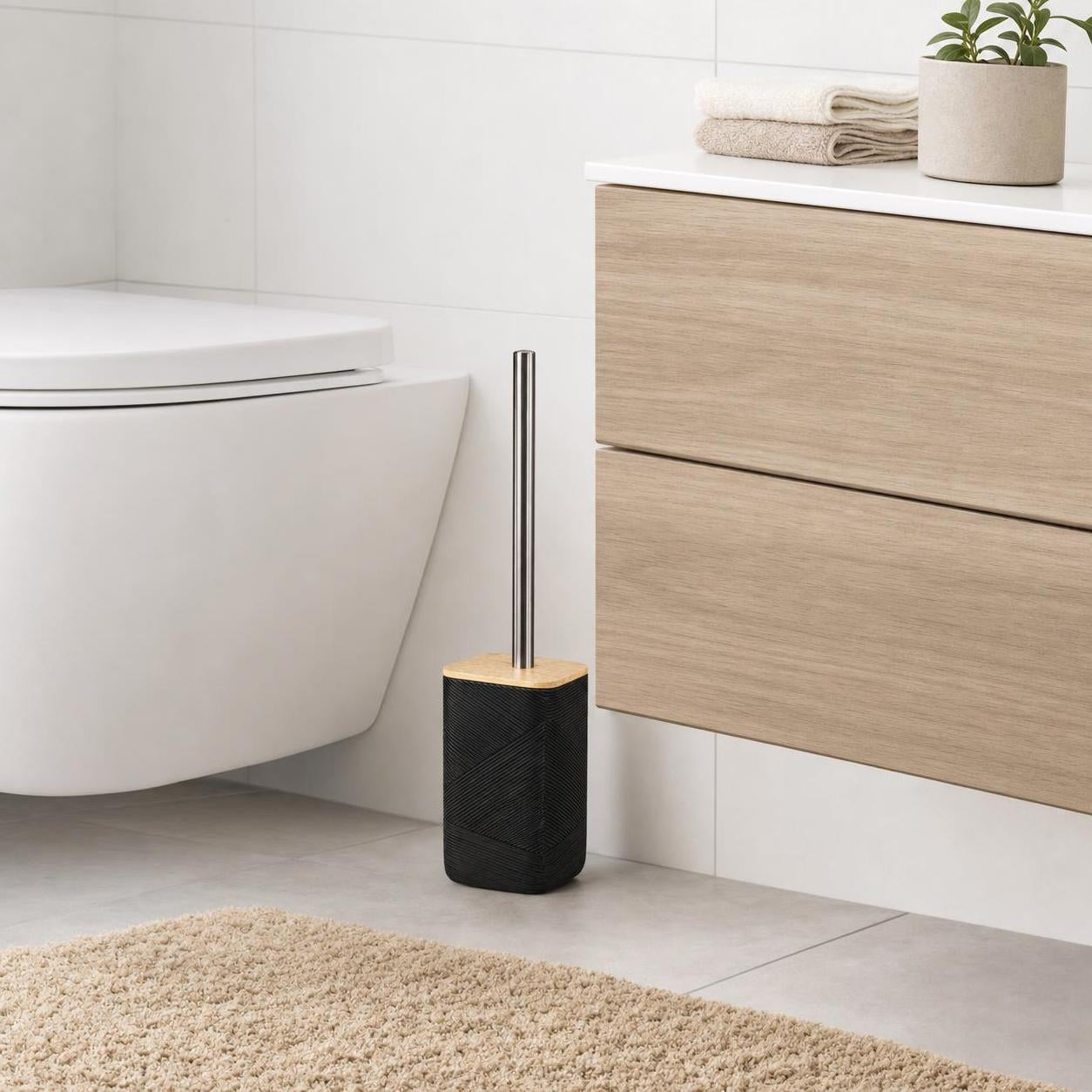 Eine schwarze WC-Bürste steht neben Toilette und Holzwaschtisch.